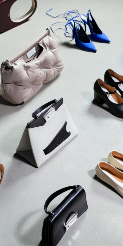 High-angled shot of stylish shoes and bags arranged on a white surface, exuding elegance and luxury.